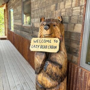 A bear statue holding a sign saying " welcome to easy bear cabin ".