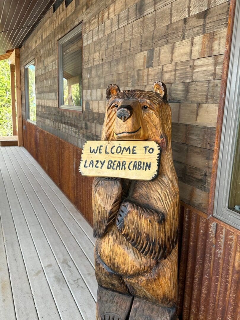 A bear statue holding a sign saying " welcome to easy bear cabin ".